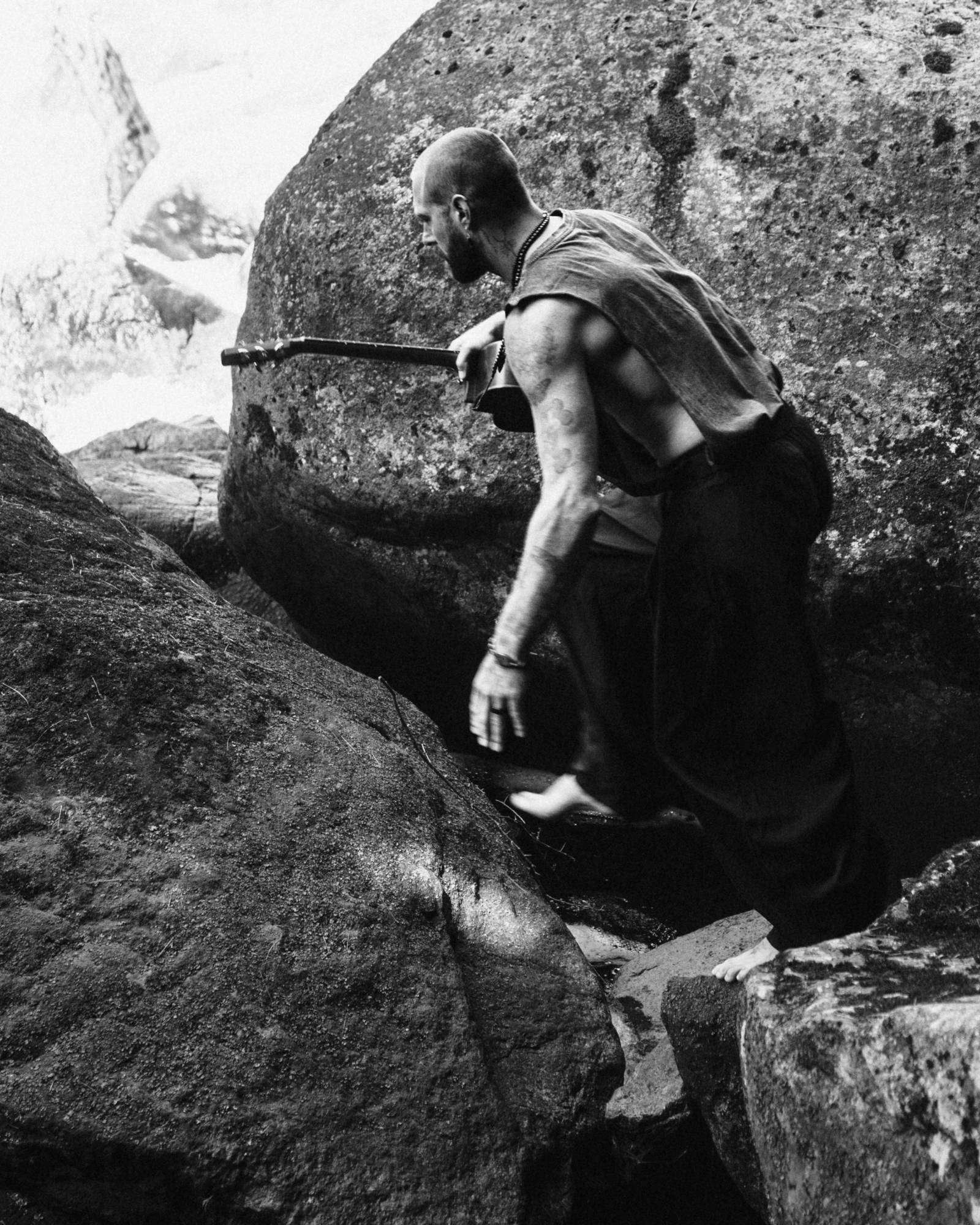 Jonathan Roy climbing between boulders with his guitar, black and white
